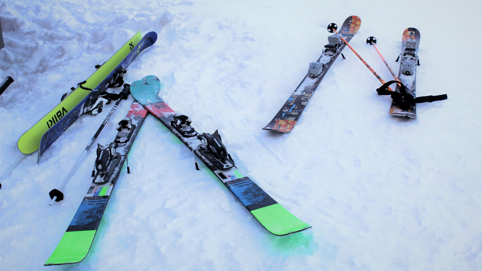 Three pairs of skis and poles laid on snow.