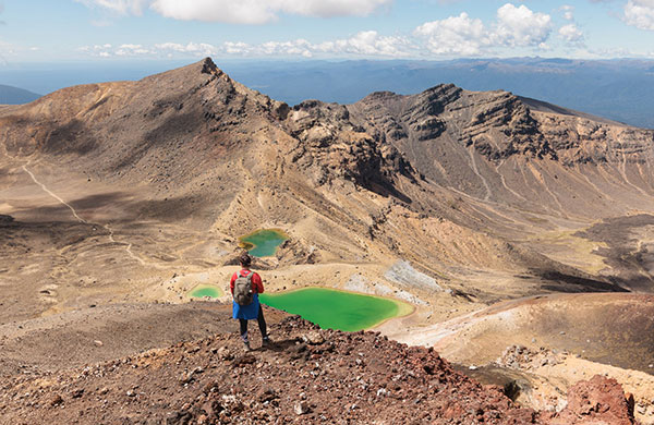 Hiker with backpack standing in front of one Tongariros Emerald lakes.