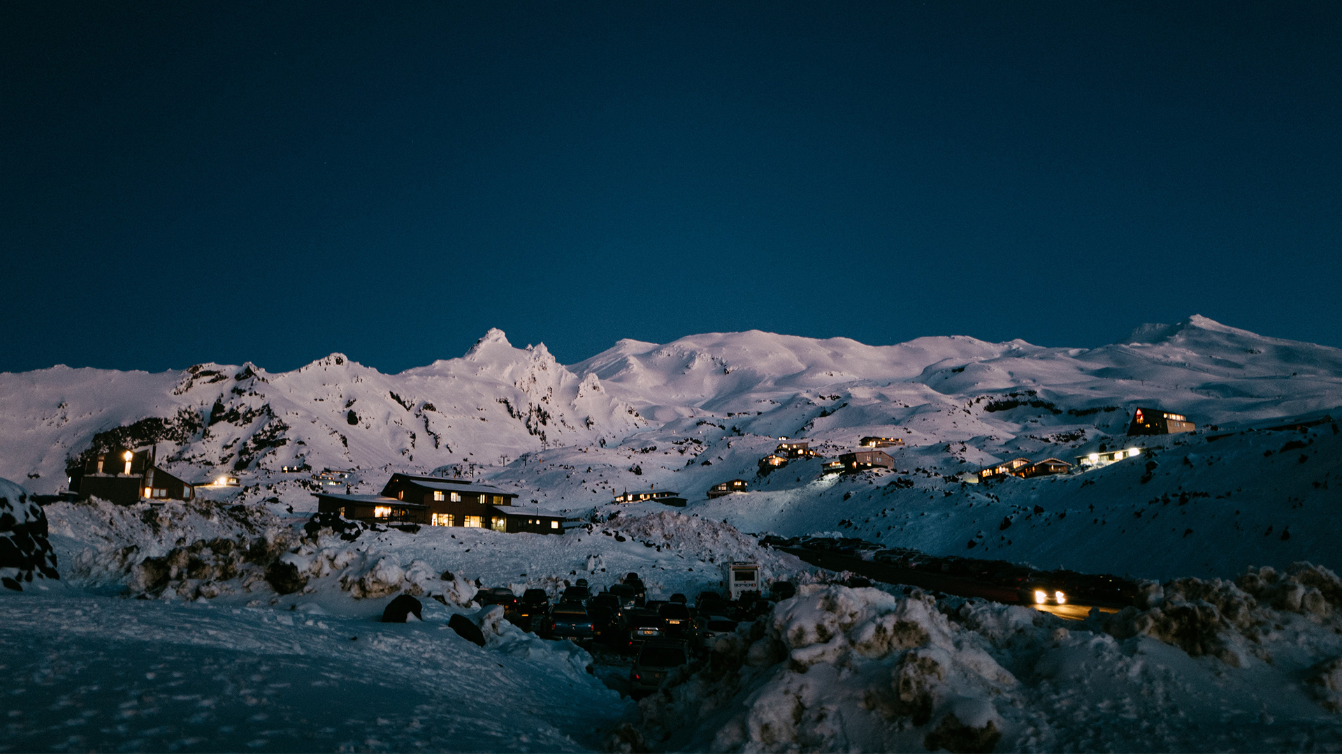 Homes with lights on scattered amongst snow covered mountains at night. 